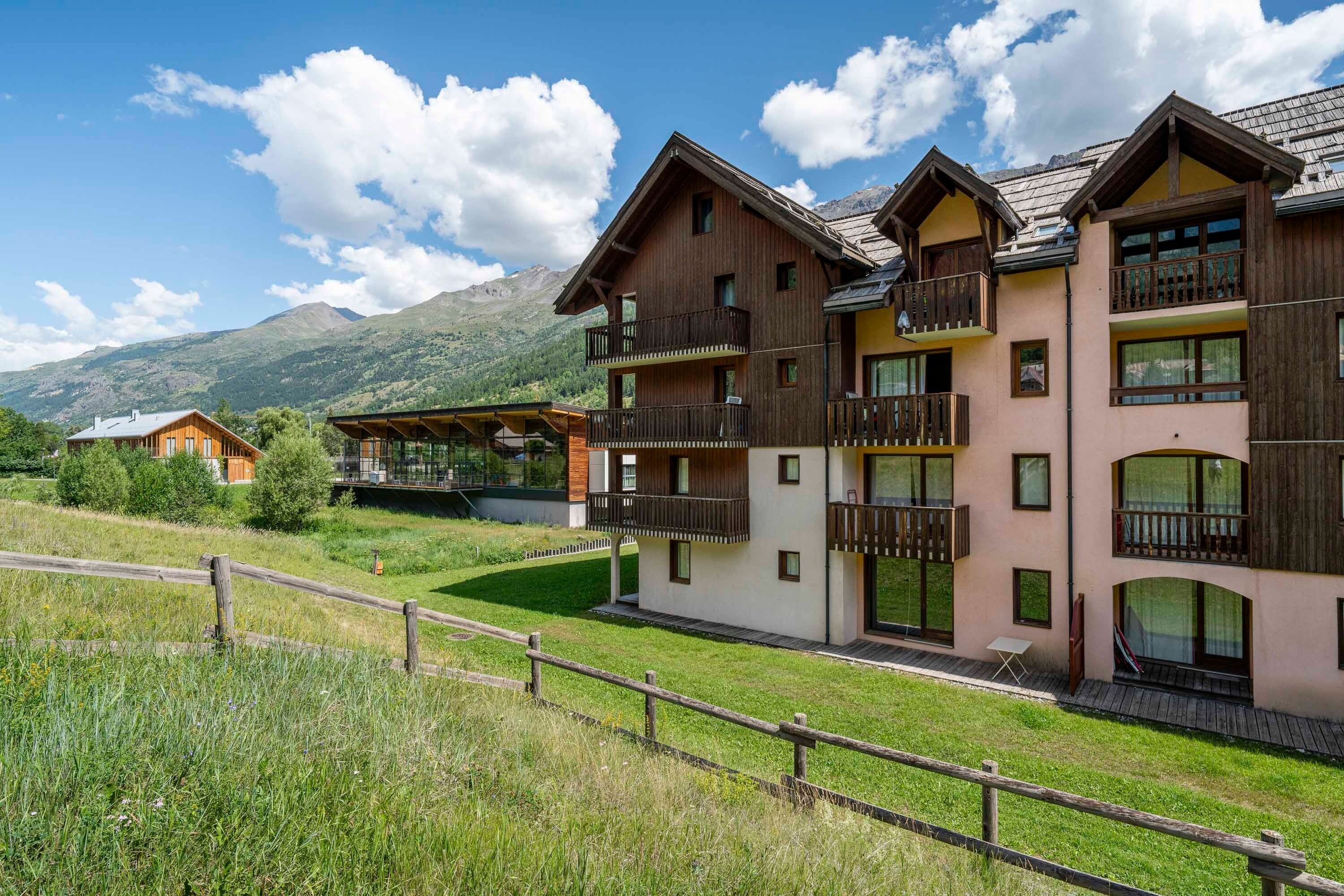 A multi-story building with balconies, a wooden fence, and a mountainous backdrop.