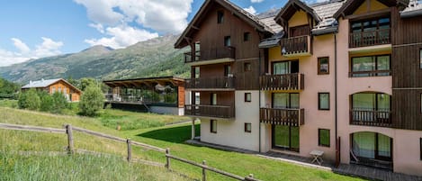 A multi-story building with balconies, a wooden fence, and a mountainous backdrop.