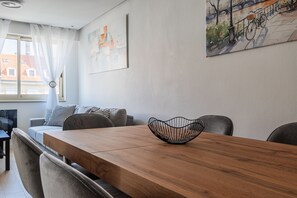 Una sala de estar moderna con una mesa de comedor de madera, un sofá gris y un cuadro de un paisaje urbano.