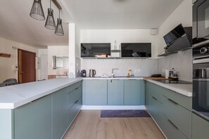 A modern kitchen with light blue cabinets, a white countertop, and pendant lighting. - Perle de Strasbourg - Bel appt pour 4 avec balcon (Strasbourg)