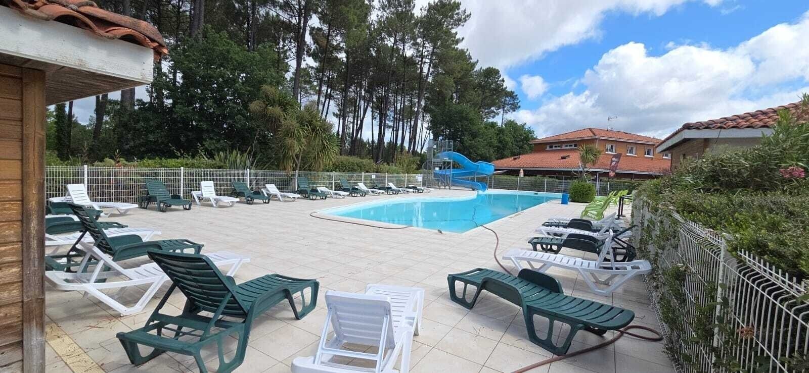 Un espace piscine comprenant des chaises longues, un toboggan et une piscine clôturée.
