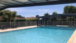 Una piscina trasparente con zona coperta, circondata da una recinzione e sedie.