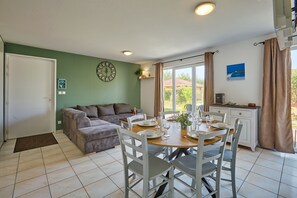 A cozy living room with a sofa, a dining table set for four, and a kitchen area with a microwave. - La Parenthèse Bleue - À 5 min à pied de la plage (Parentis-en-Born)
