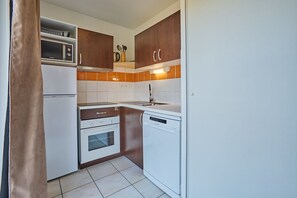 A compact kitchen with a microwave, oven, dishwasher, and wooden cabinets. - La Parenthèse Bleue - À 5 min à pied de la plage (Parentis-en-Born)