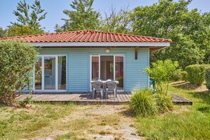 A light blue house with a red-tiled roof, a wooden deck, and a small patio with two chairs. - La Parenthèse Bleue - À 5 min à pied de la plage (Parentis-en-Born)