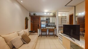 Un espacio habitable pequeño con sofá, televisor, zona de cocina y comedor.