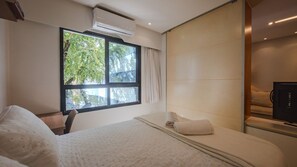 Una habitación de hotel con un ventanal grande, una cama, un televisor y un aire acondicionado de pared.
