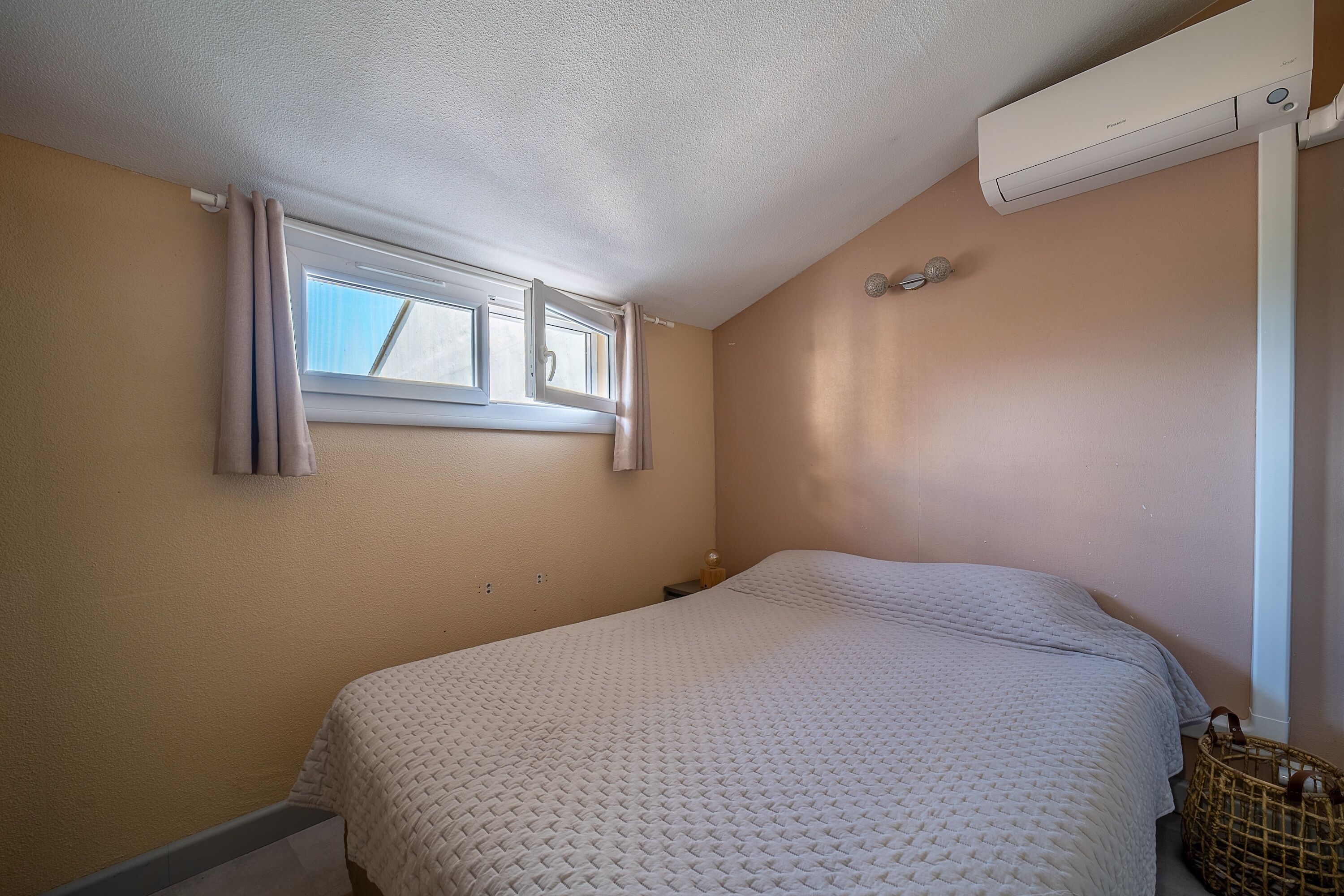 Ein Schlafzimmer mit Bett, Fenster, Klimaanlage und einem kleinen Nachttisch.