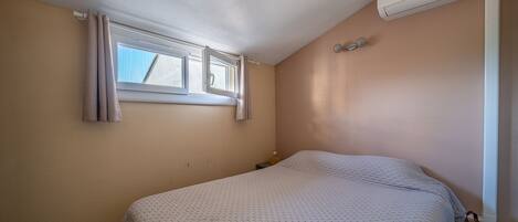 Une chambre à coucher avec un lit, une fenêtre, un appareil de climatisation et une petite table de chevet.