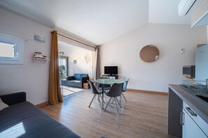 Ein modernes Wohnzimmer mit Sofa, einem Esstisch mit Stühlen, einer Küchenzeile und einem großen Fenster mit Vorhängen.