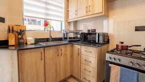 A kitchen with wooden cabinets, a gas stove, a microwave, and a window with blinds. - Tranquil 2-bedroom apartment in welcoming Nairobi neighborhood (Nairobi)
