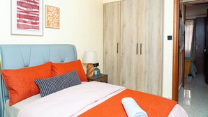 Quarto de hotel com cama, guarda-roupa, mesa de cabeceira e porta que dá para outro espaço.