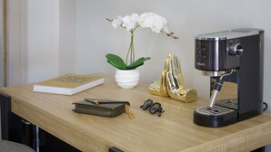 Uma mesa de madeira com uma cafeteira, um livro, uma planta, um par de óculos de sol e um objeto dourado decorativo.
