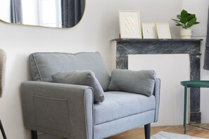 A grey sofa with cushions, a small green side table, a white fireplace, and a mirror on the wall.