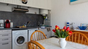 Een kleine keuken met een wasmachine, een koffiezetapparaat en een eethoek met een vaas tulpen.