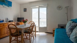 Een kamer met een eettafel, stoelen, een televisie, een bank en een raam met uitzicht.