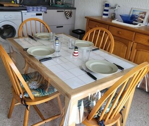 A dining table set with plates, cutlery, and glasses, surrounded by wooden chairs with patterned cushions. - Le Petit Nid de Saint Pierre - À 100 m de la plage (Fleury)
