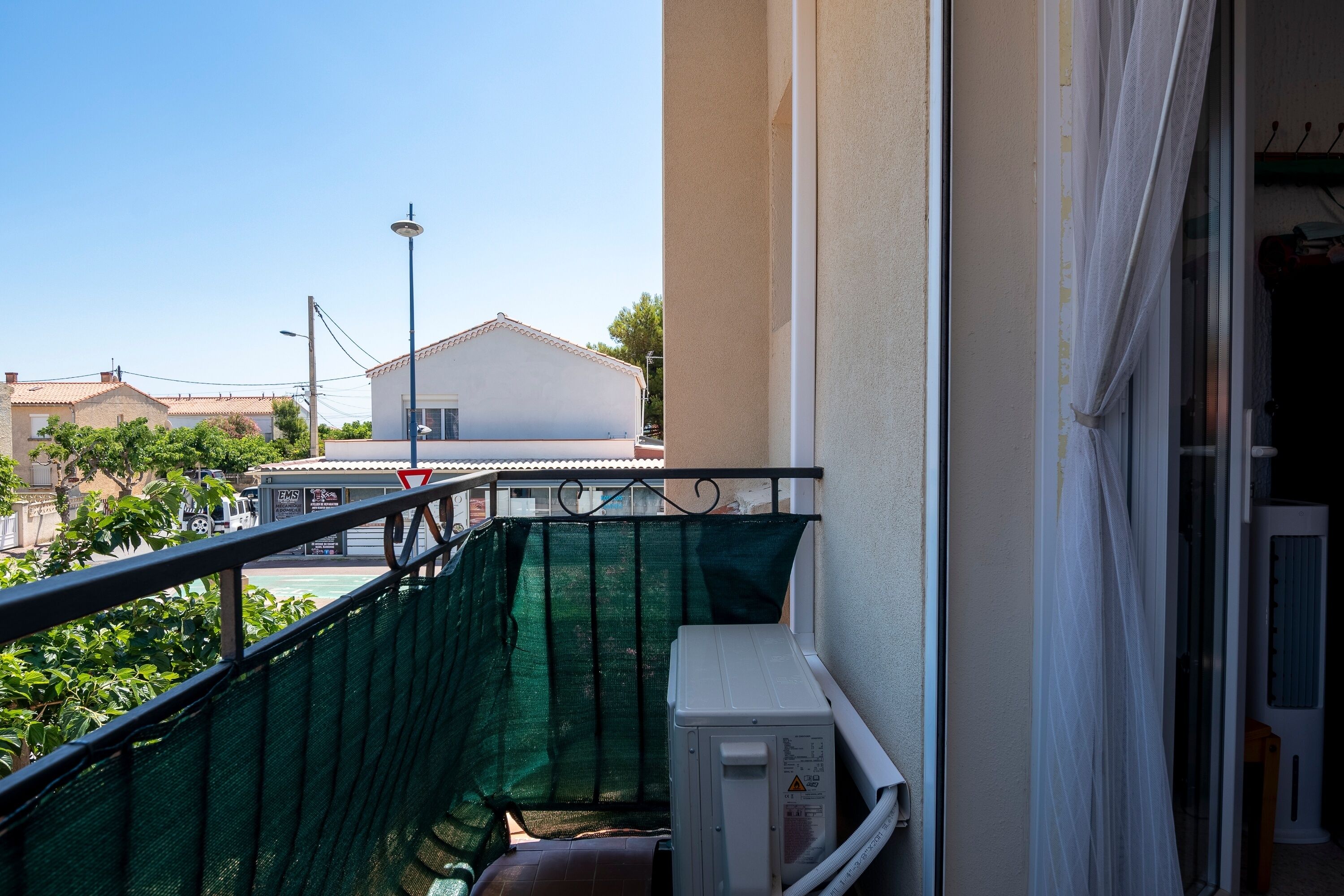 A balcony with a green safety net, a white air conditioning unit, and a view of a building with a red roof in the background.