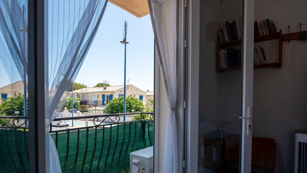 Een balkon met uitzicht op gebouwen, een groene netbarrière en een witte radiator.