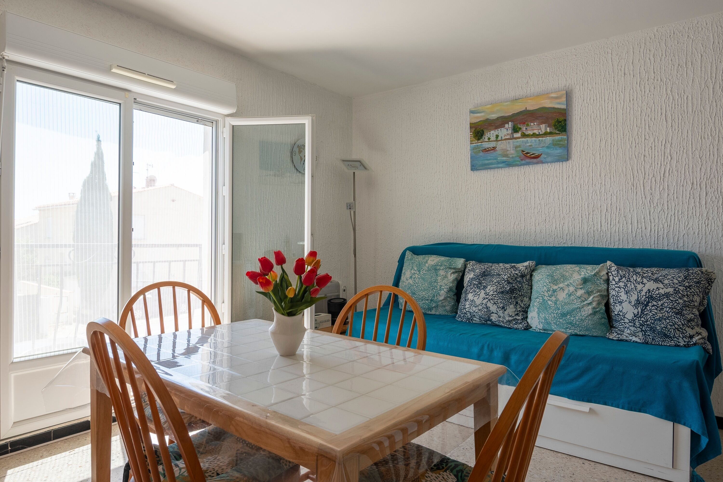 A room with a dining table, chairs, a sofa, and a painting on the wall.