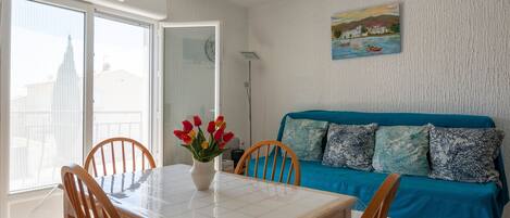 A room with a dining table, chairs, a sofa, and a painting on the wall.