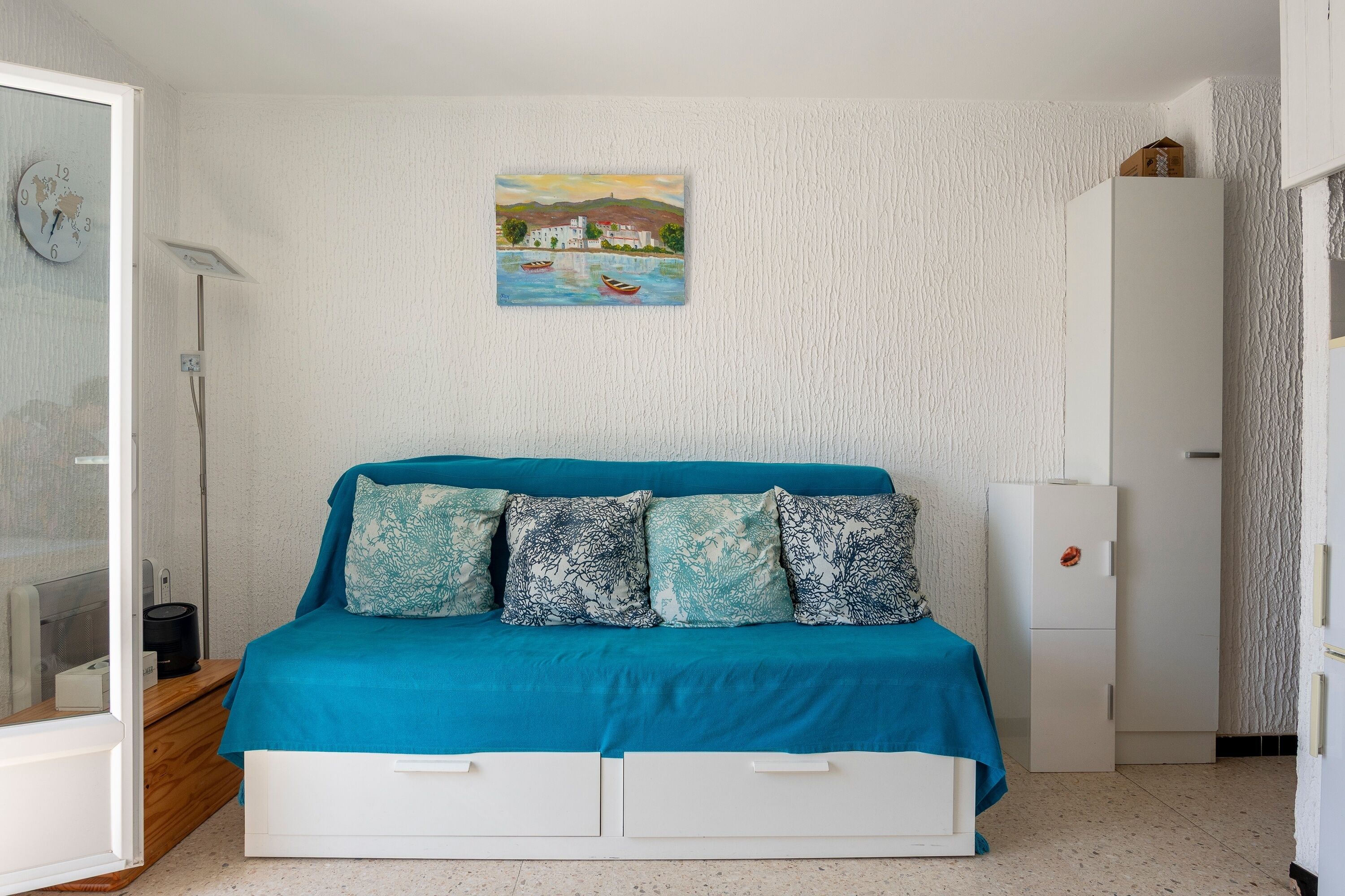 Een slaapkamer met een bed, een schilderij, een witte garderobe en een wit kastje.