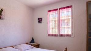 Een slaapkamer met een bed, nachtkastje, lamp, raam met gordijnen en een klein schilderij aan de muur.