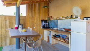 A wooden pergola-covered outdoor kitchen with a table, chairs, and a refrigerator. - Le Clos des Plaisirs - Studio avec jacuzzi privé (Carcassonne)