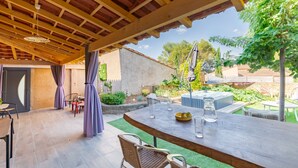An outdoor patio with a wooden pergola, a table with chairs, and a hot tub in the background. - Le Clos des Plaisirs - Studio avec jacuzzi privé (Carcassonne)