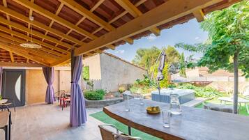 Une terrasse extérieure dotée d’une pergola en bois, d’une table avec des chaises et d’un jacuzzi en arrière-plan.