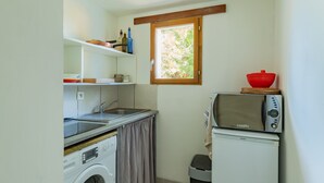 A compact kitchenette with a washing machine, a sink, a small window, and a microwave. - Le Clos des Plaisirs - Studio avec jacuzzi privé (Carcassonne)