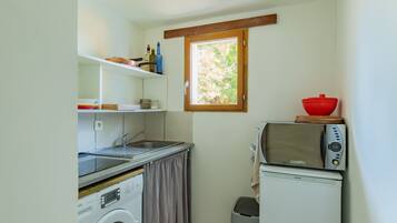 A compact kitchenette with a washing machine, a sink, a small window, and a microwave.