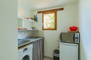 Uma cozinha compacta equipada com máquina de lavar, pia, uma pequena janela e micro-ondas.