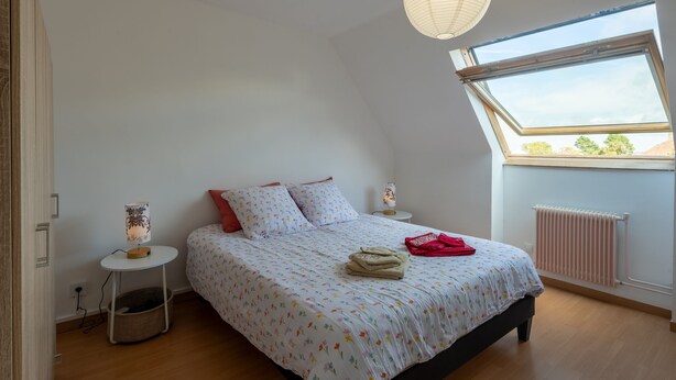 Ein Schlafzimmer mit Bett, Nachttisch, Lampe, Heizkörper und Fenster.