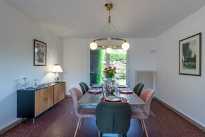 Een eetkamer met een tafel gedekt voor zes personen, een kast met decoratieve objecten, en uitzicht op groen buiten.