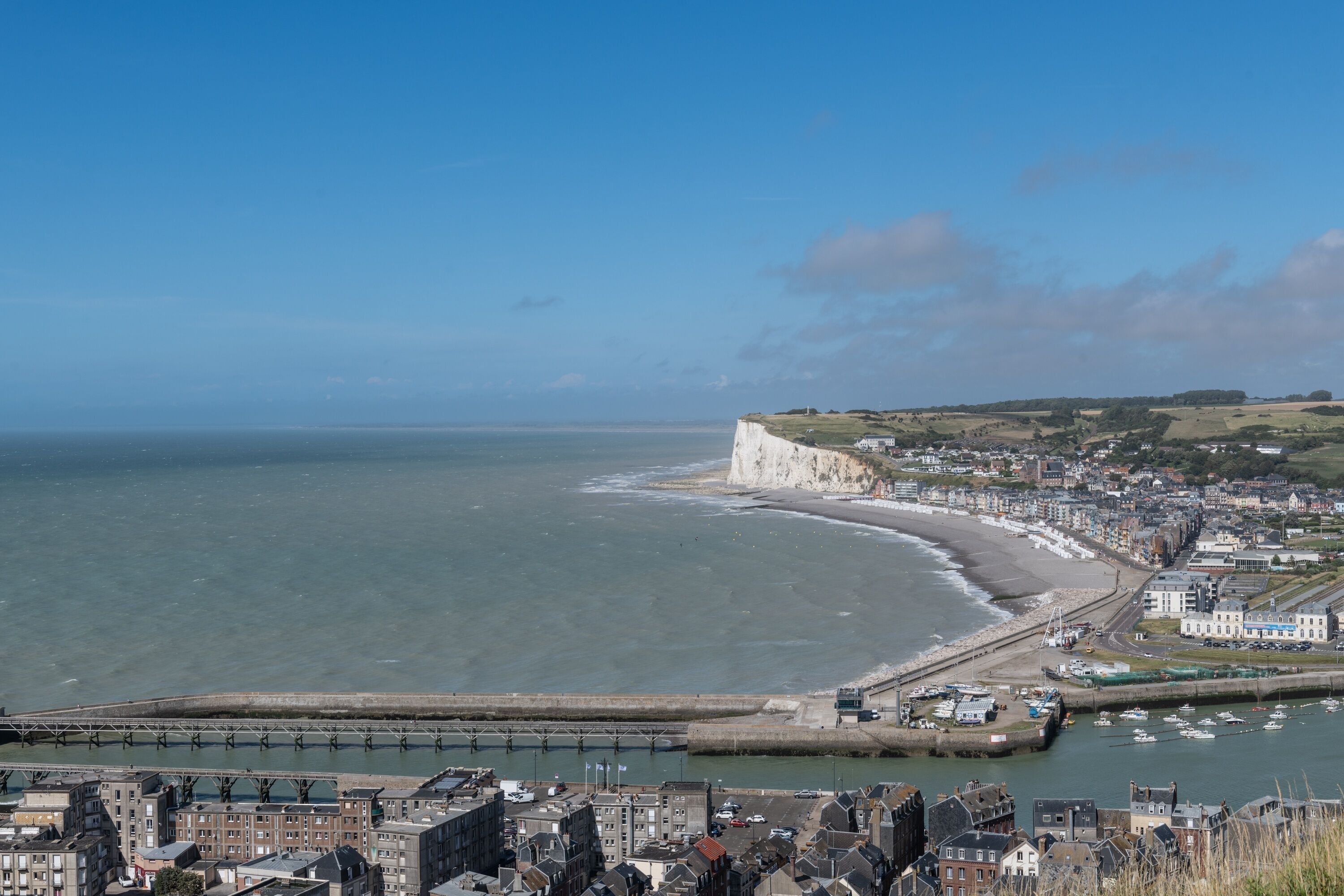 A coastal town with a prominent cliff, a harbor with boats, and a bridge.