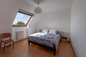 A bedroom with a skylight, a bed with a floral bedspread, a red chair, and a bedside table with a lamp. - Le Nid d'Albâtre - À 2 km de la plage (Le Tréport)