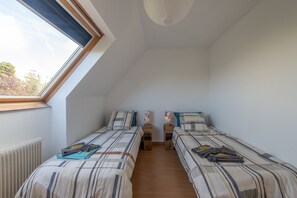 Een kamer met twee eenpersoonsbedden, een raam, een radiator en een plafondlamp.