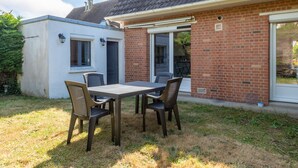 Eine Terrasse mit Tisch und Stühlen, ein Backsteinhaus mit einer Schiebetür und ein kleines, weißes Gebäude.