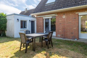 Eine Terrasse mit Tisch und Stühlen, ein Backsteinhaus mit einer Schiebetür und ein kleines, weißes Gebäude.