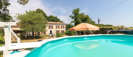 A swimming pool with a white deck, a brown umbrella, and a house in the background.