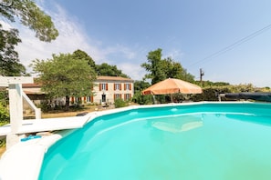 Ein Pool mit einer weißen Liegefläche, einem braunen Sonnenschirm und einem Haus im Hintergrund.