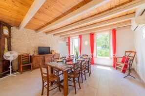 A dining area with a wooden table and chairs, a television, and a stone wall.