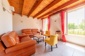 A furnished living room with a wooden ceiling, a sofa, a chair, a coffee table, and a view through large windows.