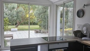 A modern kitchen with a large island, sliding glass doors to a patio, and a view of a garden. - 220 m² Charente-style farmhouse with a garden and terrace (Berneuil)