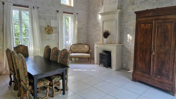 A dining room with a large table and chairs, a fireplace, and a wooden cabinet. - 220 m² Charente-style farmhouse with a garden and terrace (Berneuil)