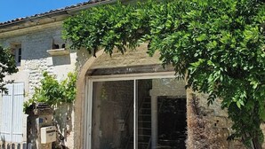 A stone building with a tiled roof, a glass door entrance, and a small garden area with potted plants. - 220 m² Charente-style farmhouse with a garden and terrace (Berneuil)