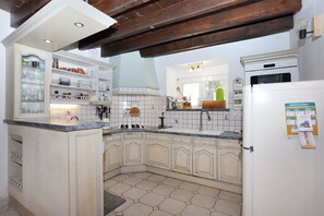 Eine Küche mit integrierter Kochinsel, weißen Schränken, einem Kühlschrank und einer gefliesten Spritzschutzwand.
