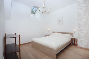 Ein Schlafzimmer mit einem hölzernen Bett, einem kleinen Tisch, einem Nachttisch, einer Kronleuchter, einem Fenster und einer Wand mit Blätermotiv.