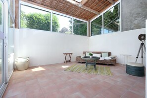A sunlit room with a large window, a wicker sofa, a small table, and a tripod. - Au Coeur des Landes Bretonnes - Maison pour 6 (Bains-sur-Oust)